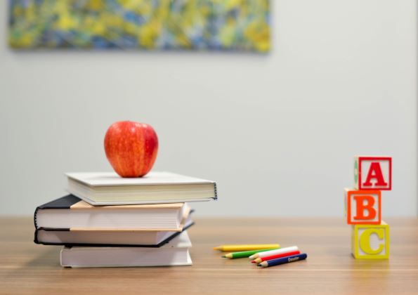 school books on table with apple on top